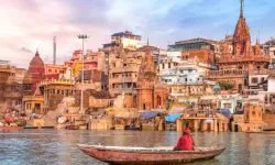 Ancient Varanasi city architecture and Ganges river ghat at sunset with view of an Indian sadhu sitting a boat on the river Ganges.
